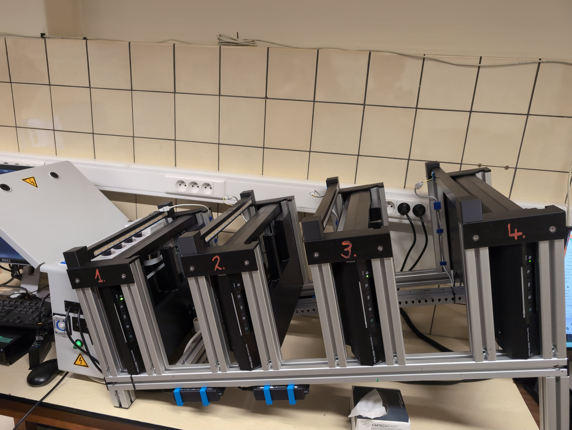 A metal frame holding 4 scanners in place, sitting in a lab. On the left there is an electrical box where the LED controls and Arduinos are housed.